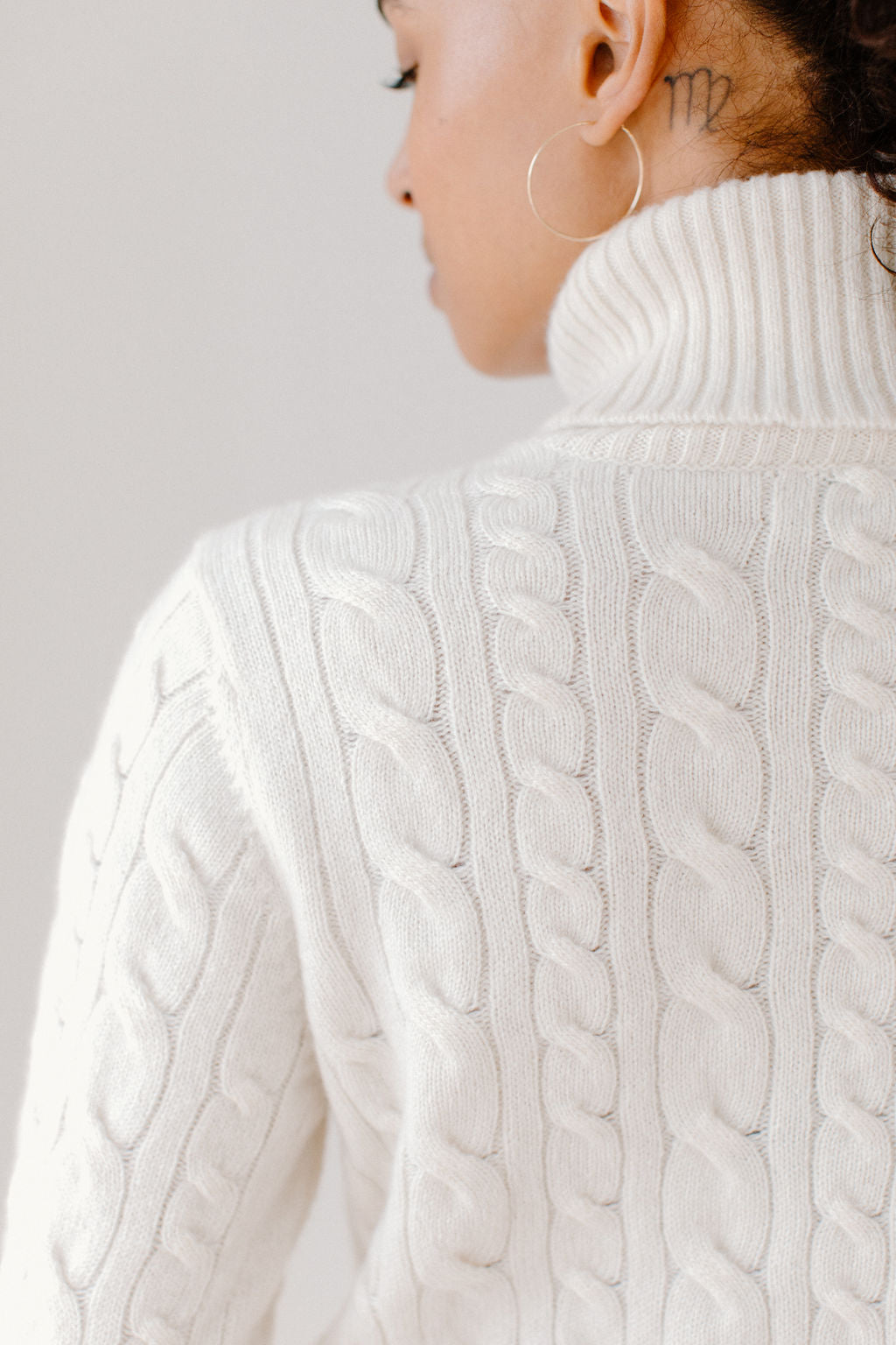 Close up of model wearing the Cream, Cable-Knit Turtleneck sweater against a white background to show the sweater&#39;s design and texture.