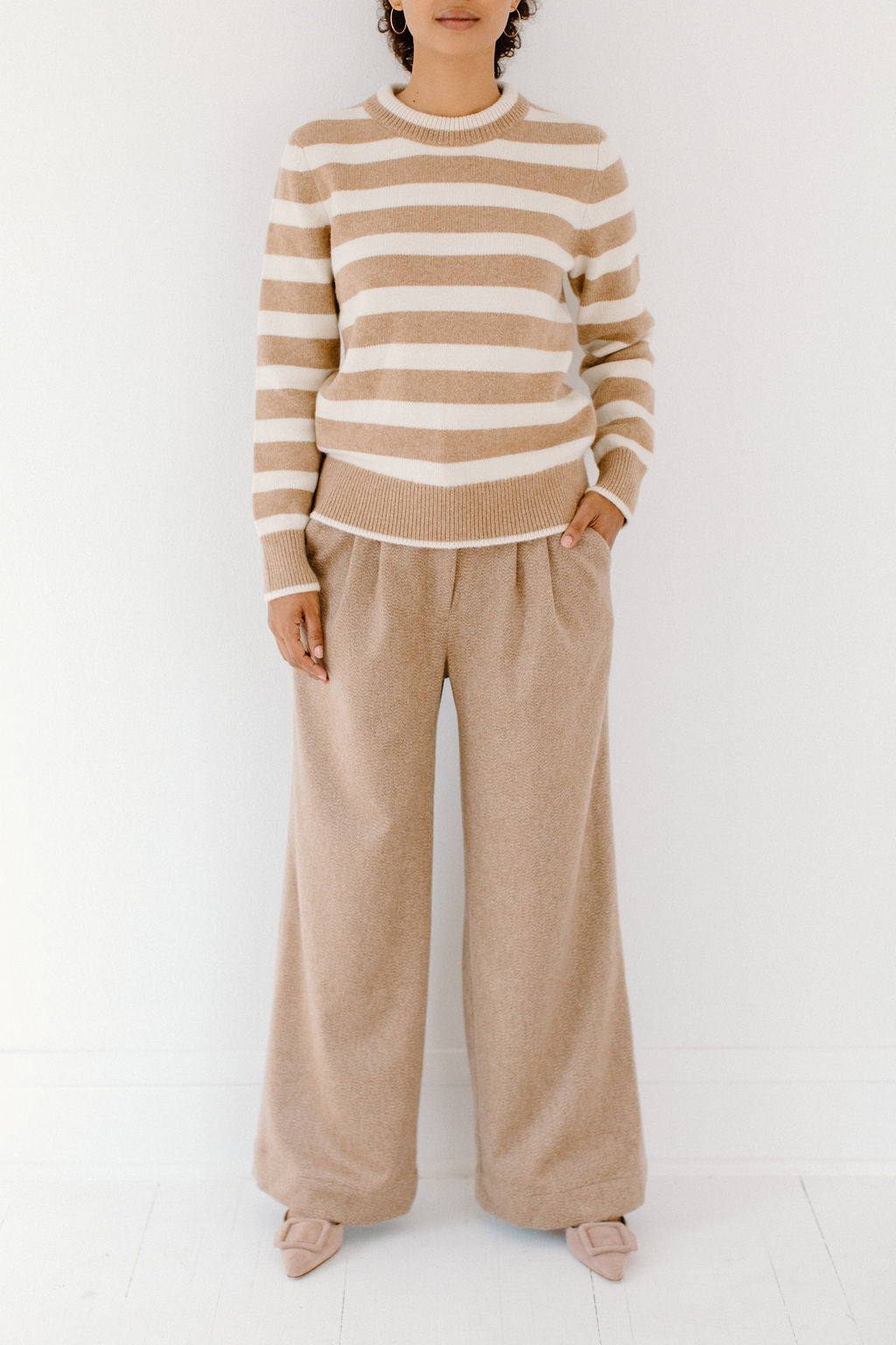 Model wearing the camel/cream Classic Striped Cashmere Crew, paired with wide-leg camel trousers and beige flats, on a white background.