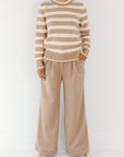 Model wearing the camel/cream Classic Striped Cashmere Crew, paired with wide-leg camel trousers and beige flats, on a white background.