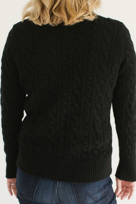 Back view of Eleanor Leftwich in the Black Cable-Knit Turtleneck sweater paired with dark denim against a white background.