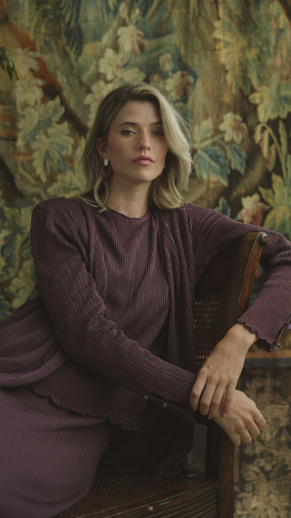 Woman modeling a pleated silk purple cardigan on a floral backdrop