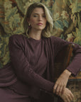 Woman modeling a pleated silk purple cardigan on a floral backdrop