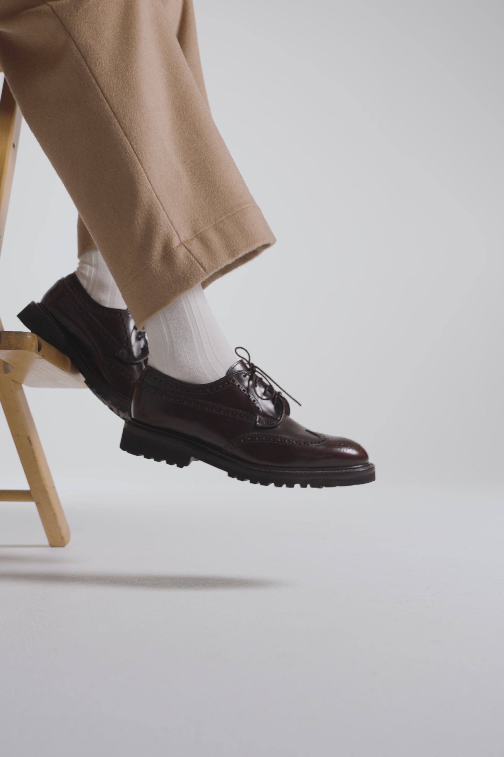 Model wearing dark chocolate European shoes while sitting on a stool