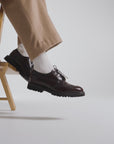 Model wearing dark chocolate European shoes while sitting on a stool
