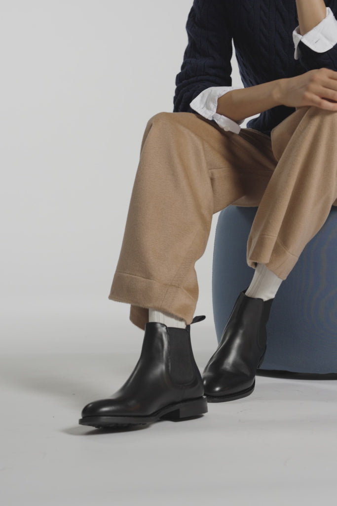 A woman wearing black boots sitting on a blue ottoman in a white studio