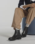 A woman wearing black boots sitting on a blue ottoman in a white studio