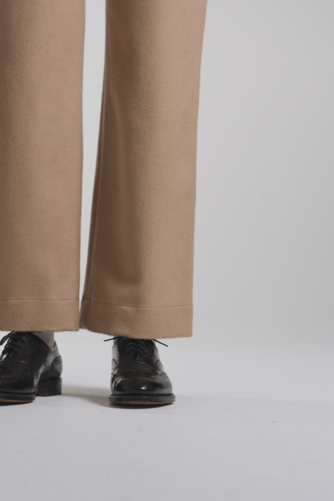 Woman wearing tan pants and modeling black oxford shoes on a white backdrop