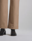 Woman wearing tan pants and modeling black oxford shoes on a white backdrop