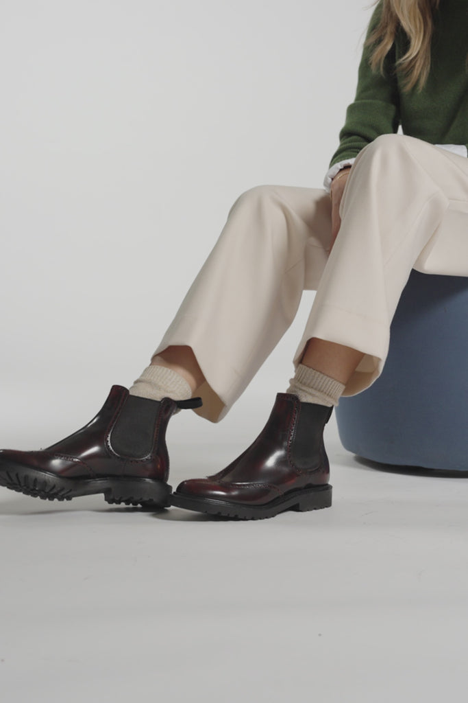 Video of a woman modeling burgundy ankle boots and cream pants on a white background