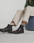 Video of a woman modeling burgundy ankle boots and cream pants on a white background