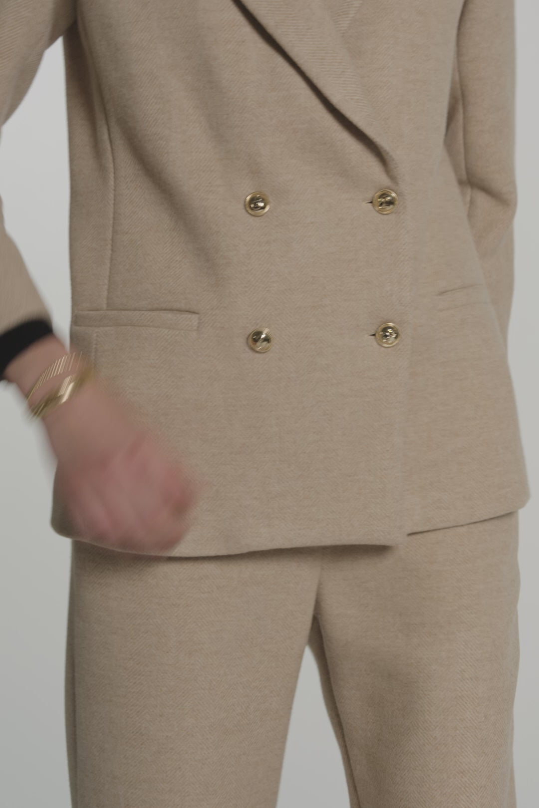 Woman modeling a tan blazer with gold buttons on a white background
