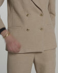 Woman modeling a tan blazer with gold buttons on a white background
