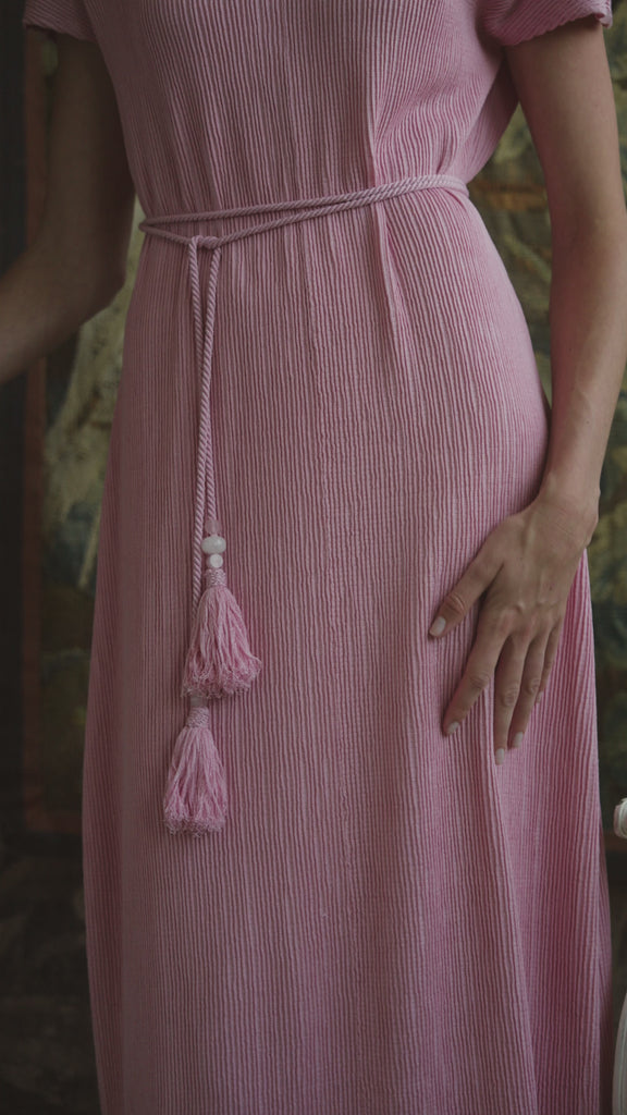 A video of a woman modeling a pleated silk dress on a patterned backdrop