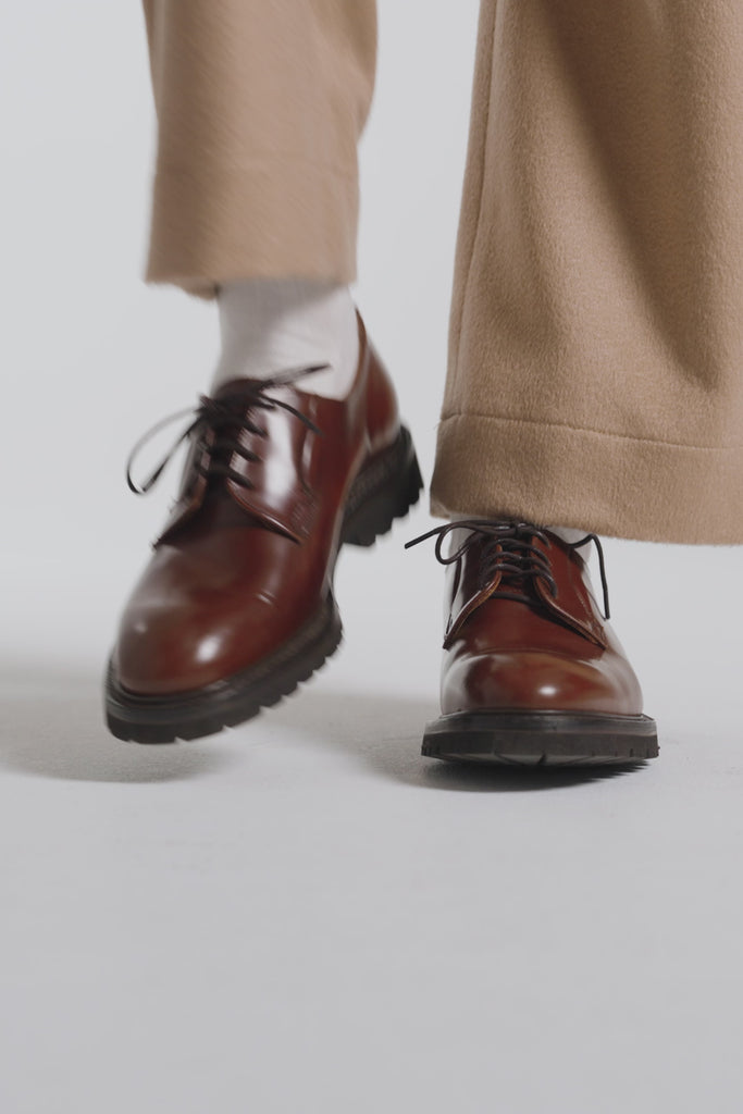 Woman modeling hazelnut color derby shoes on a white backdrop