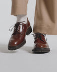 Woman modeling hazelnut color derby shoes on a white backdrop