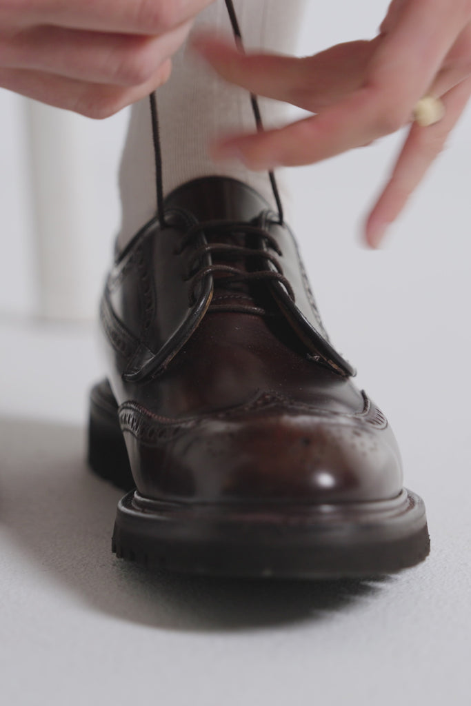 Woman tying derby shoes and wearing white socks on a white backdrop