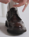 Woman tying derby shoes and wearing white socks on a white backdrop
