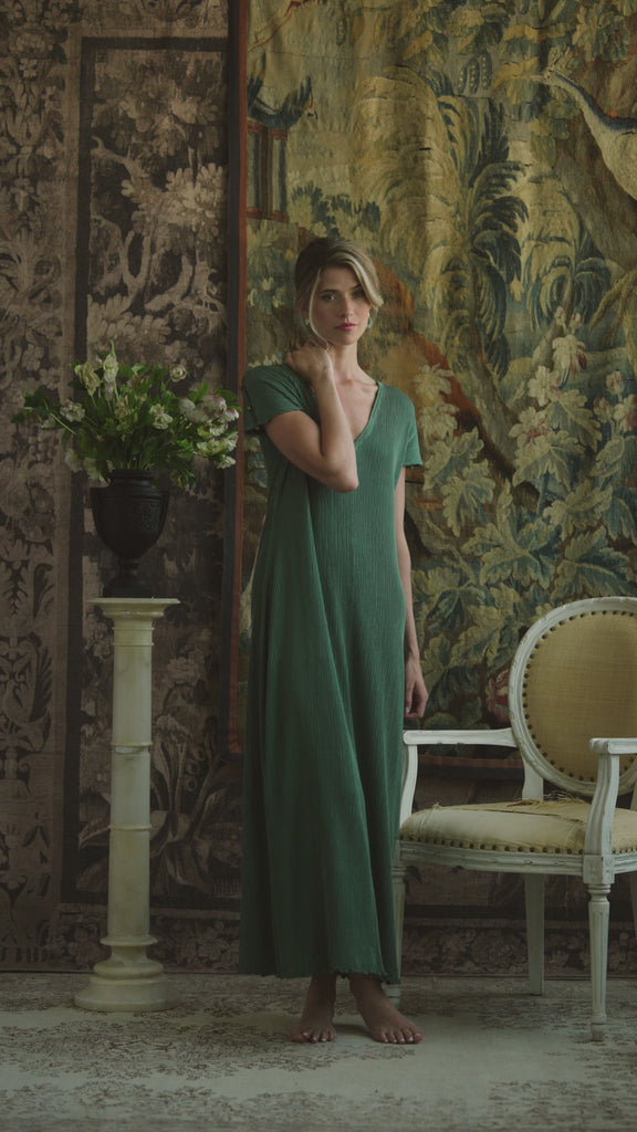 Woman modeling a silk green pleated dress on a patterned background