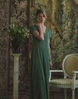 Woman modeling a silk green pleated dress on a patterned background
