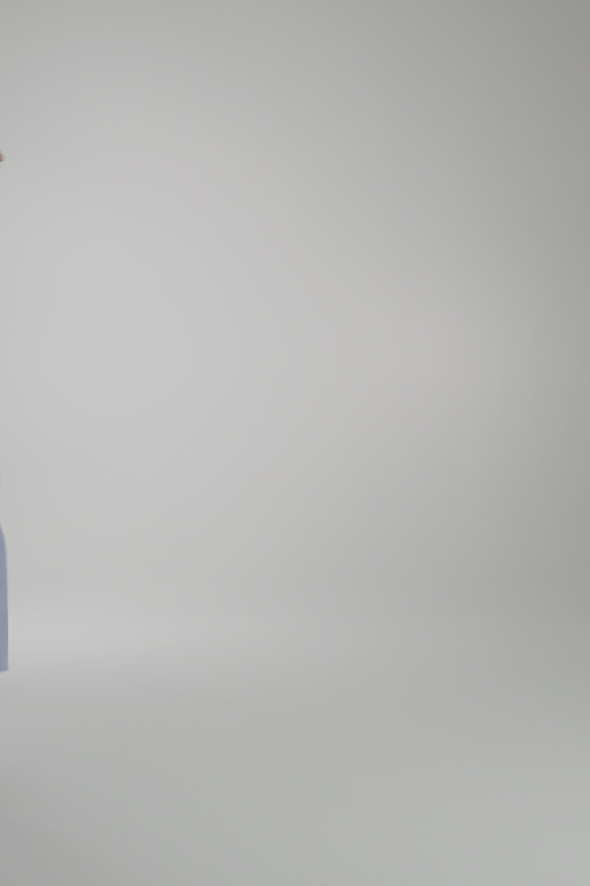 Woman wearing long blue dress with white stripe on a light gray backdrop