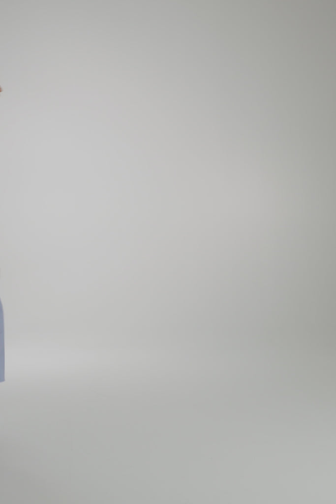 Woman wearing long blue dress with white stripe on a light gray backdrop