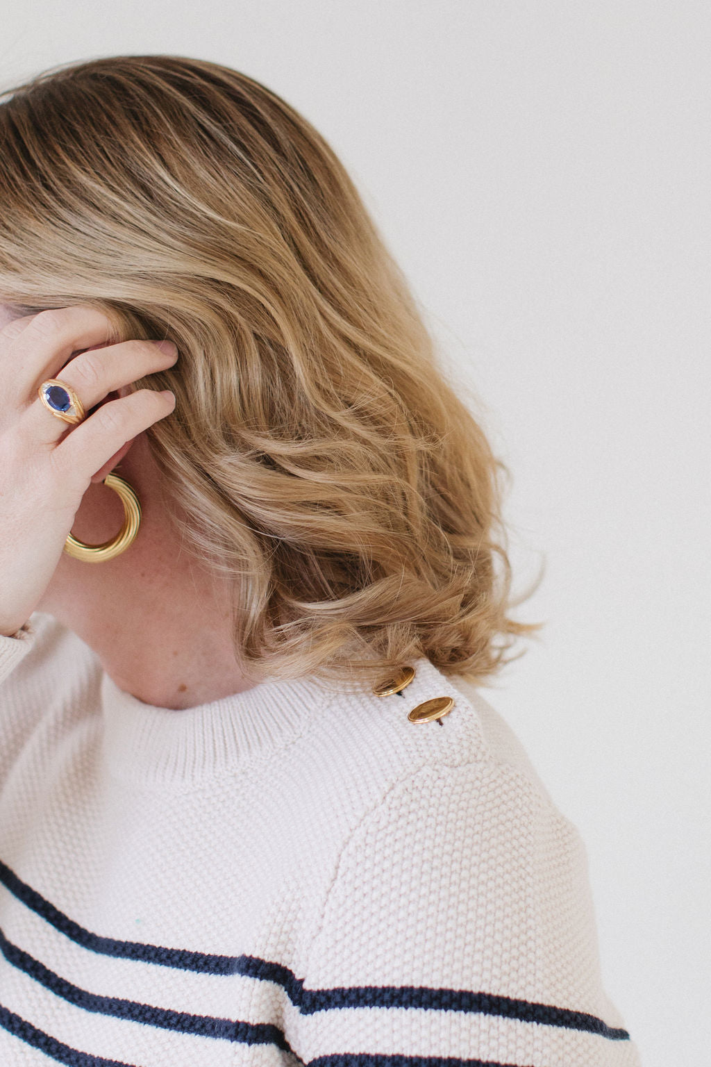 Close-up of EL wearing the Perfect Striped Crewneck in cream with navy mariner stripes, highlighting the handcrafted Italian gold buttons.
