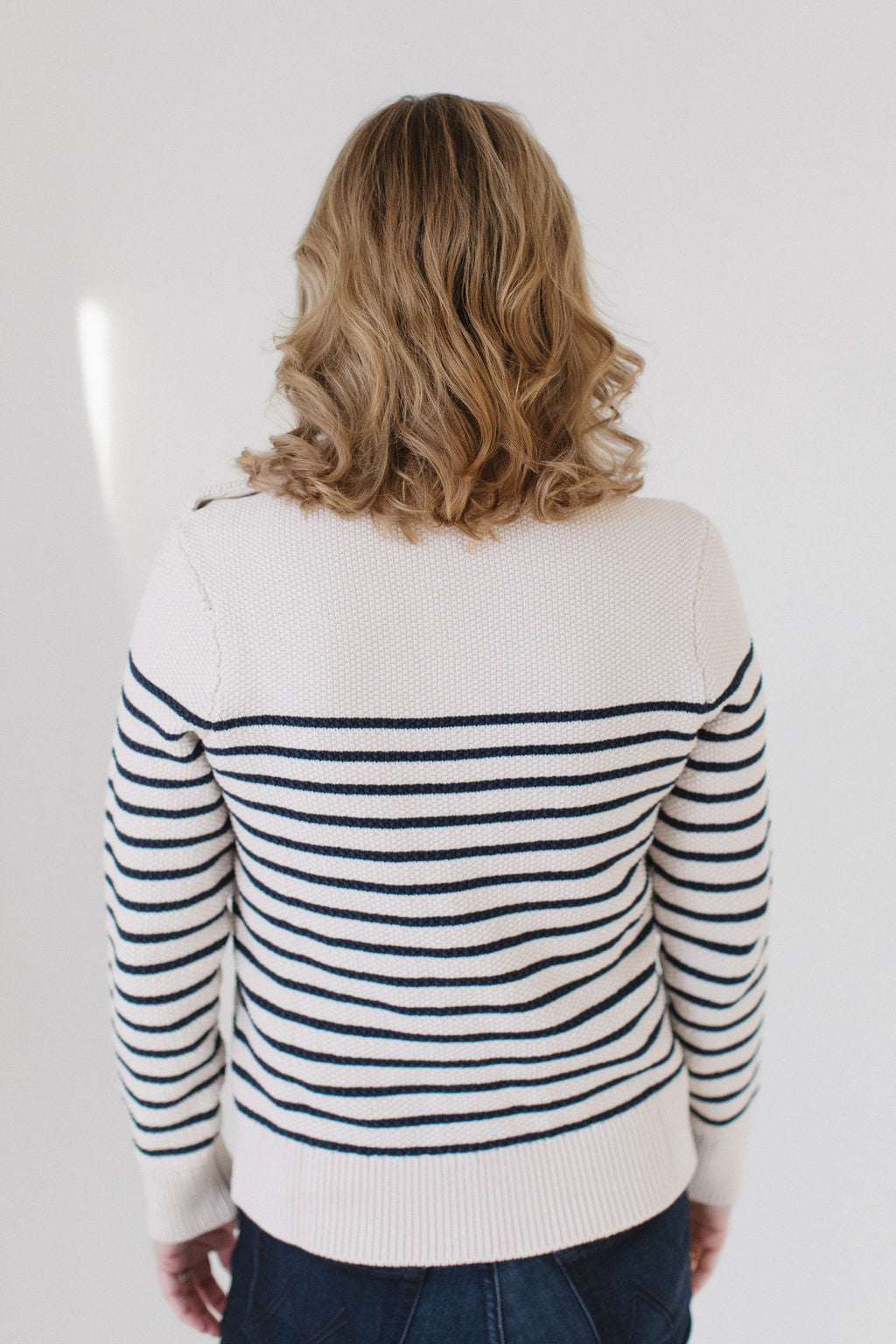 Back view of EL wearing the Perfect Striped Crewneck in cream with navy mariner stripes, paired with dark denim against a white background.