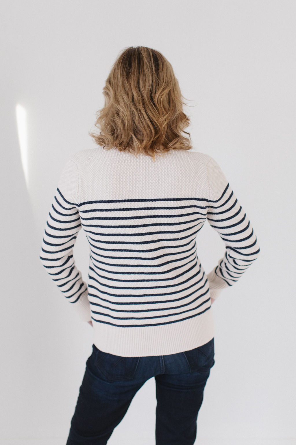 Back view of Eleanor Leftwich wearing The Perfect Striped Cardigan in cream with navy mariner stripes, paired with dark jeans.