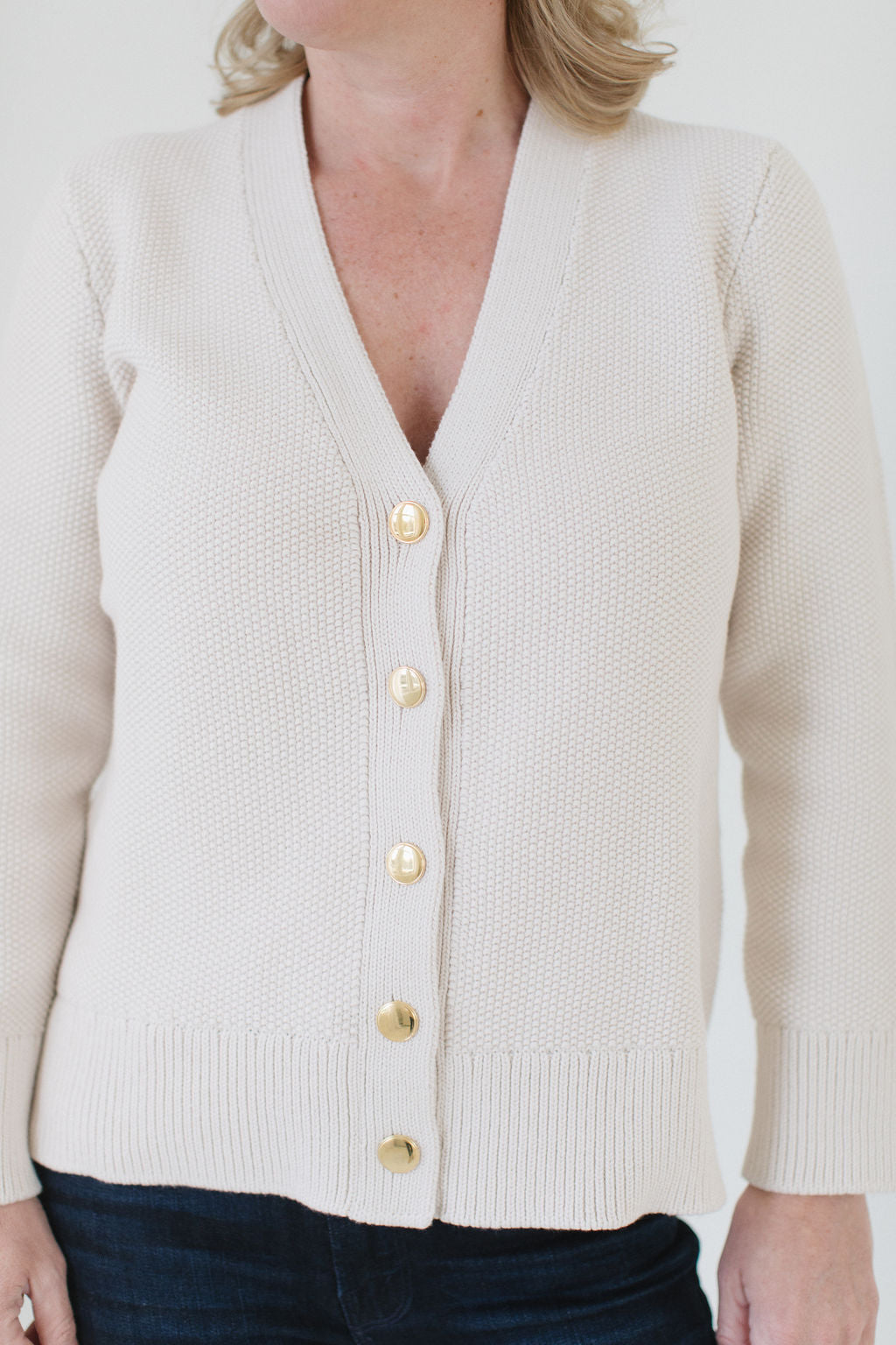 Close-up of Eleanor Leftwich wearing The Perfect Cardigan in cream, paired with jeans, and highlighting the handcrafted Italian gold buttons.