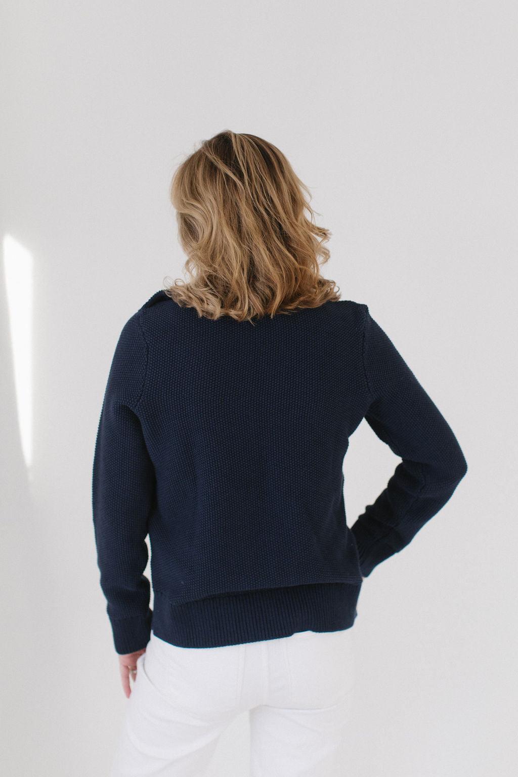 Back view of Eleanor Leftwich wearing the Navy Perfect Crewneck sweater paired with white denim jeans against a white background.