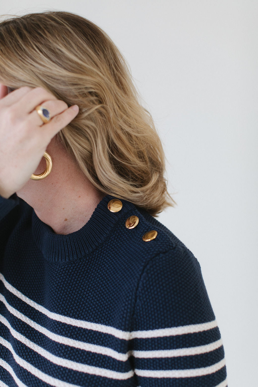 Close-up of EL wearing the Perfect Striped Crewneck in navy with cream mariner stripes, highlighting the handcrafted Italian gold buttons.