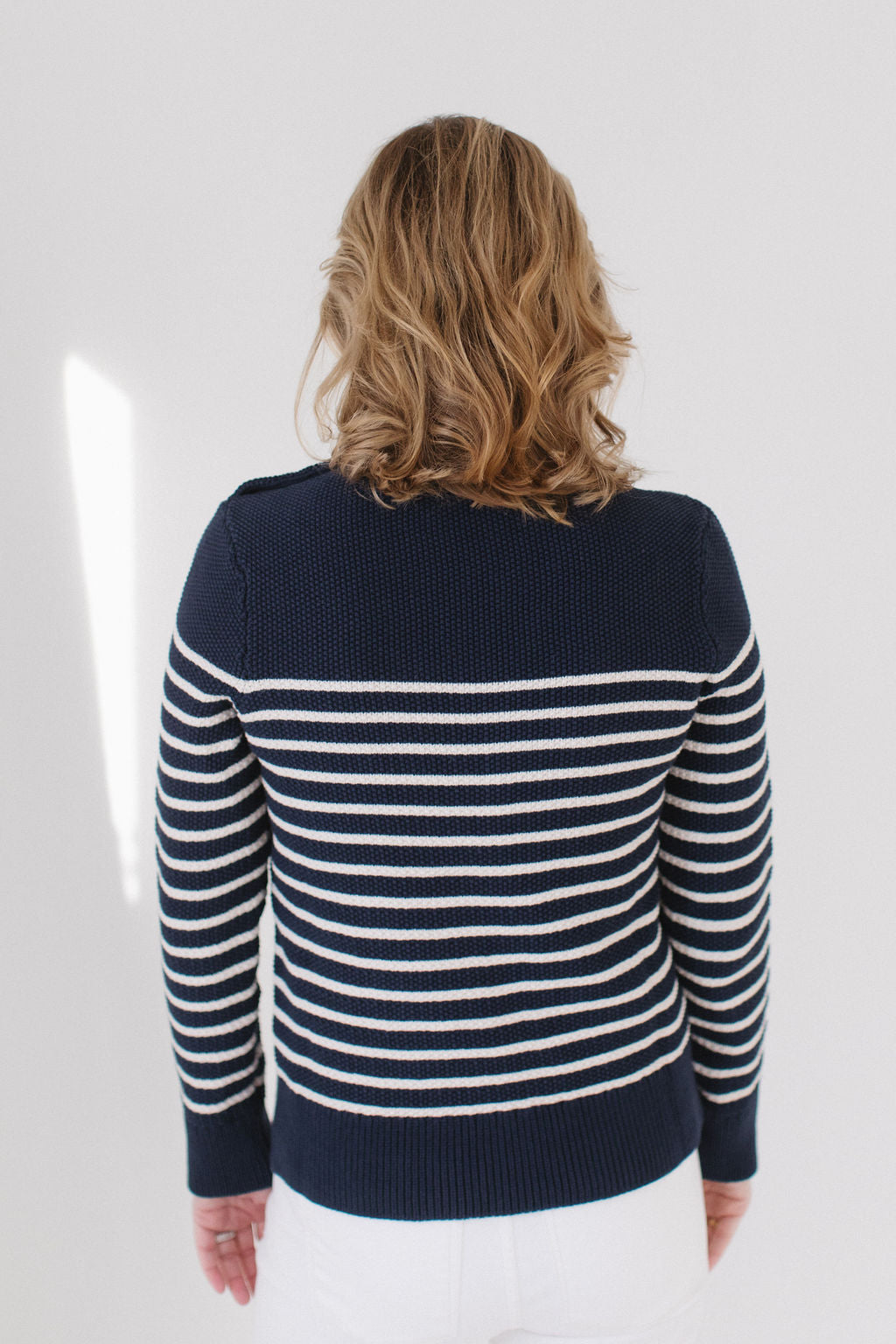 Back view of EL wearing the Perfect Striped Crewneck in navy with cream mariner stripes, paired with white jeans against a white background.