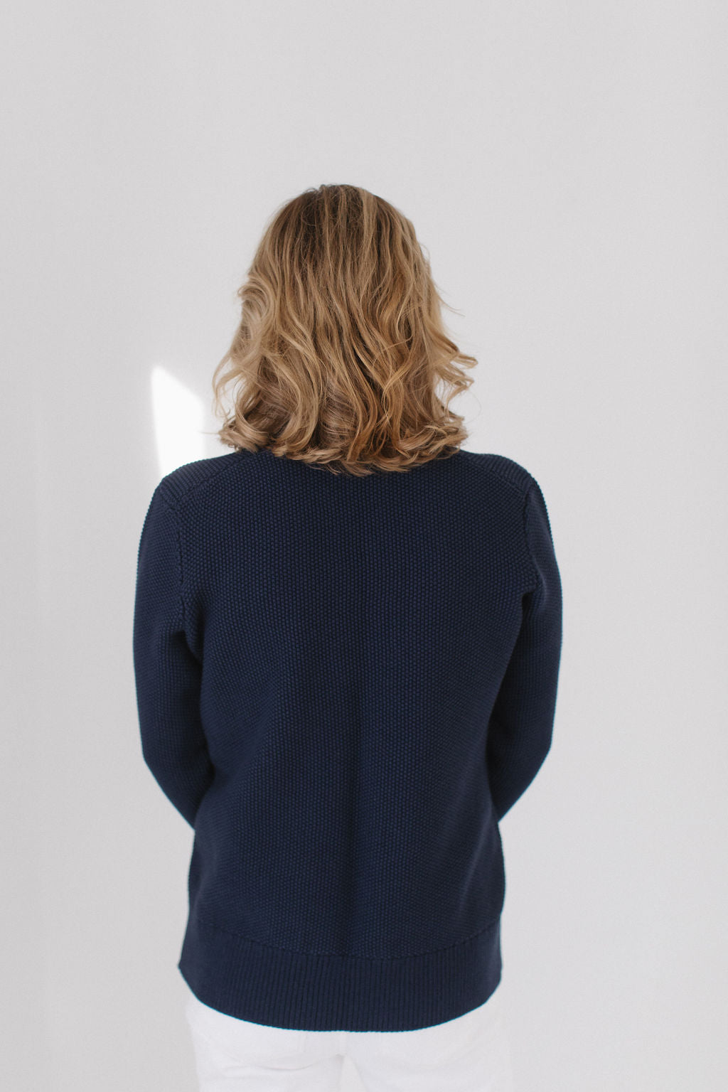 Back view of Eleanor Leftwich wearing The Perfect Cardigan in navy, paired with white jeans, and facing a white background.